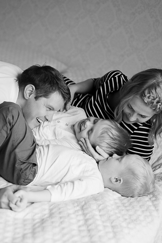 Perhe pötköttelee ja nauraa yhdessä sängyllä.